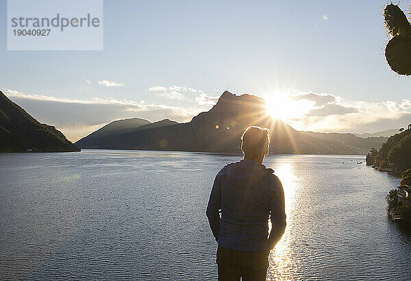 Reifer Mann beobachtet  wie die Sonne über Berg und See aufgeht
