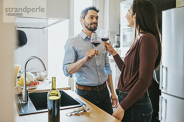 Liebespaar feiert in der Küche und stößt mit Rotwein an