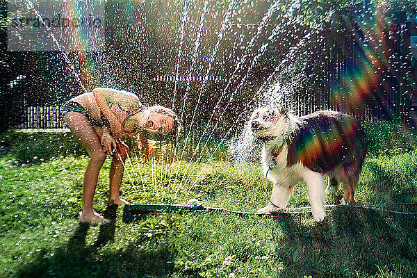 Mädchen und Hund trinken an einem heißen Sommerabend am Schlauch