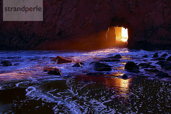 Die untergehende Sonne strahlt durch die natürliche Seebrücke im Pfiefer Beach State Park in der Nähe von Big Sur  Kalifornien; November 2009.