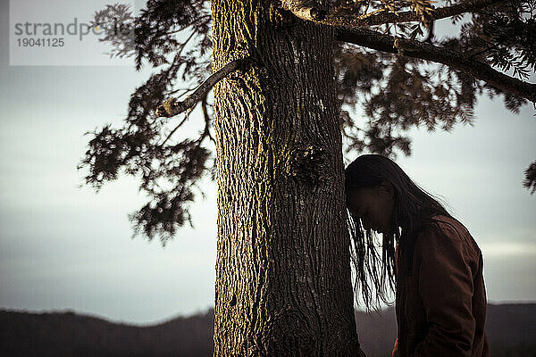 Androgyne Person lehnt Kopf an Baum