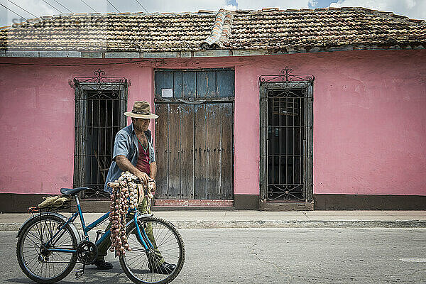 Ein einsamer kubanischer Lebensmittelhändler läuft mit seinem Fahrrad durch die rustikalen Straßen von Trinidad  Kuba