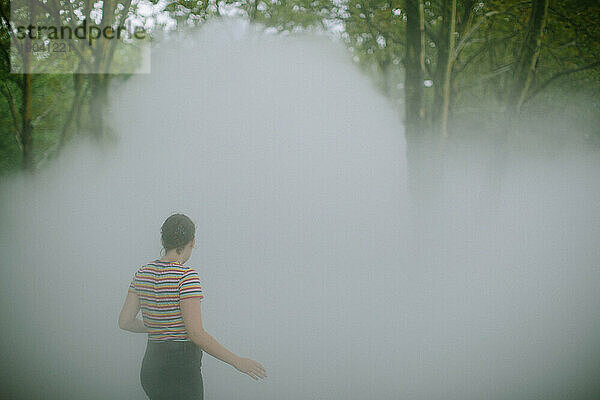 Young woman walking away through fog in a park