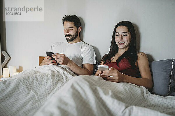 Junges Paar im Bett und schaut auf sein Smartphone