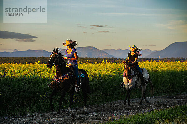 Zwei Cowgirls reiten bei Sonnenuntergang durch ein Rapsfeld