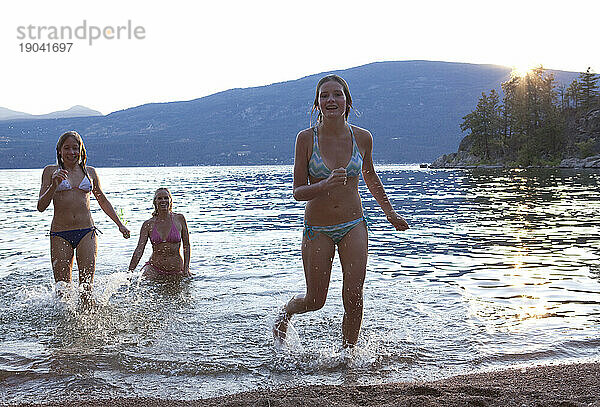 Drei Mädchen rennen bei Sonnenuntergang aus dem See