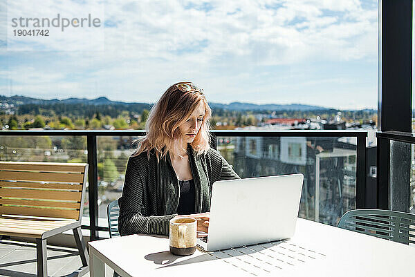 Frau arbeitet draußen auf der Terrasse am Laptop