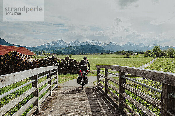A biker cross the bridge with big mountains of The Alps in the front