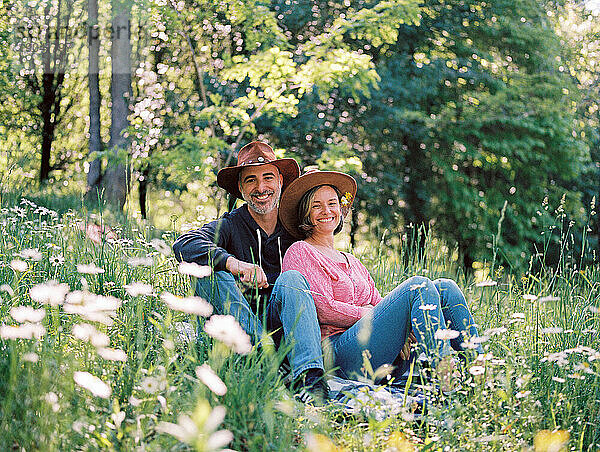 Ein Paar mittleren Alters sitzt zusammen im Gras zwischen Wildblumen