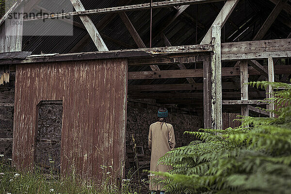 Person steht vor der Tür eines alten  verlassenen Gebäudes  das überwuchert ist