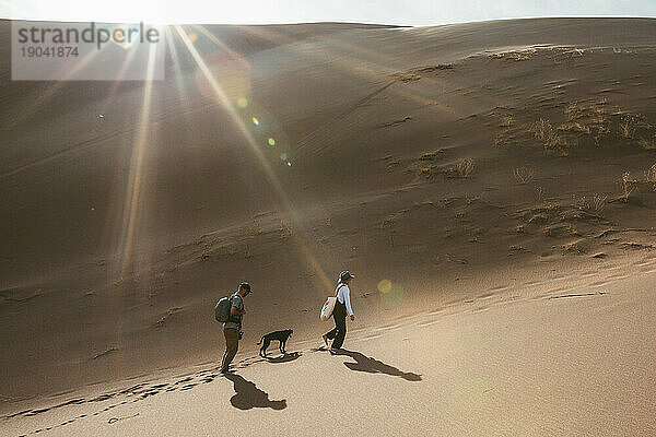 Zwei Wanderer und ihr Hund folgen Fußspuren in den Sanddünen