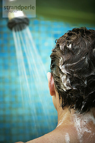 Rückansicht des Kopfes einer Frau mit Seifenlauge unter der Dusche.