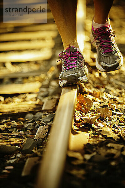 Vorderansicht der Beine einer Frau  die auf einer Eisenbahnstrecke läuft.