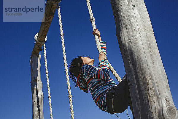 Ein entschlossenes  glückliches Kind zieht sich vor blauem Himmel an einem Seil hoch