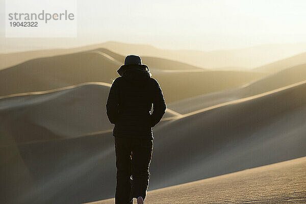 Frau in der Wüste geht dem Sonnenuntergang in den Sanddünen entgegen