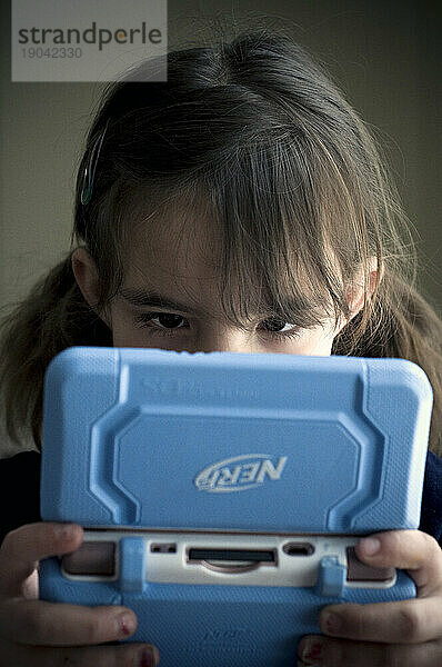 Mädchen (5-6 Jahre) spielt ein Handheld-Videospiel.