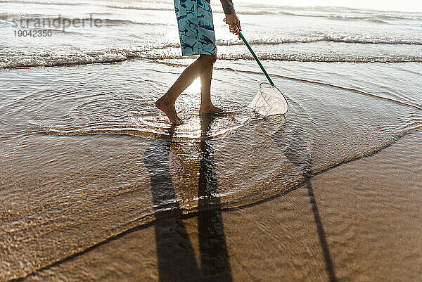 Ausgeschnittene Ansicht eines kleinen Jungen  der an einem Strand ein Netz durch das Wasser schiebt