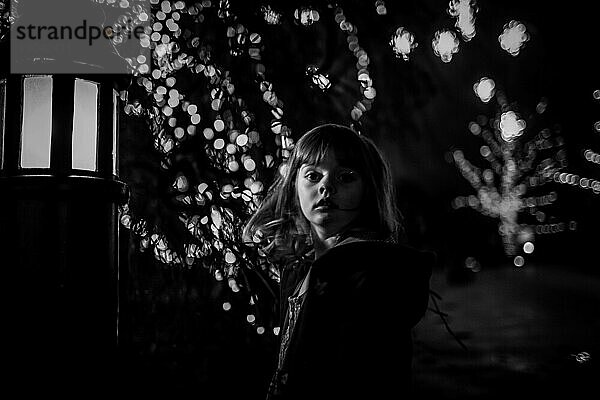 junges Mädchen in der Nacht in Schwarz und Weiß mit Bokeh und Weihnachtsbeleuchtung