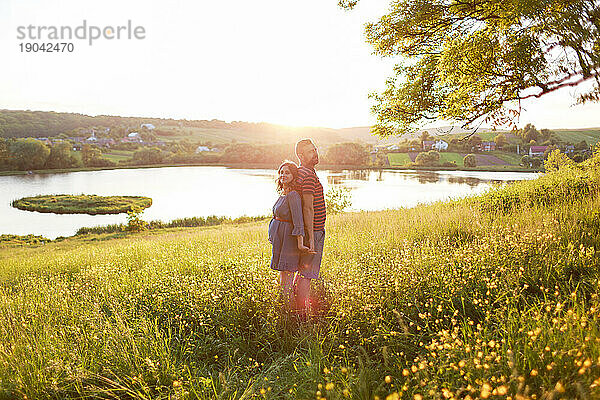 Mann und Frau stehen umarmend in einem Blumenfeld in den Strahlen der Sonne