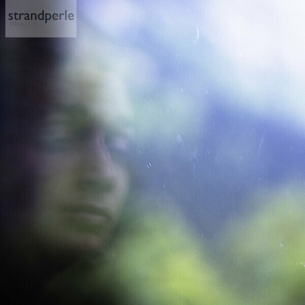 Verschwommenes Porträt einer jungen Frau in einem Fenster.