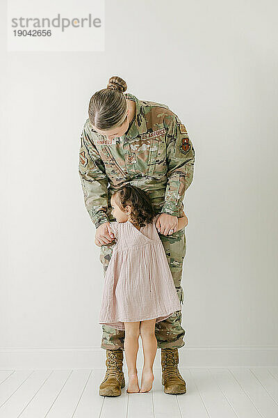 Mädchen im lila Kleid kuschelt mit Militärmutter in Uniform