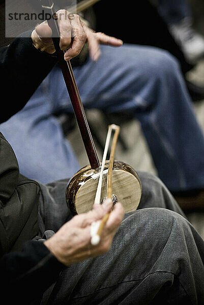 Ein älterer Mann  der auf seinen Knien ein traditionelles chinesisches Instrument spielt.