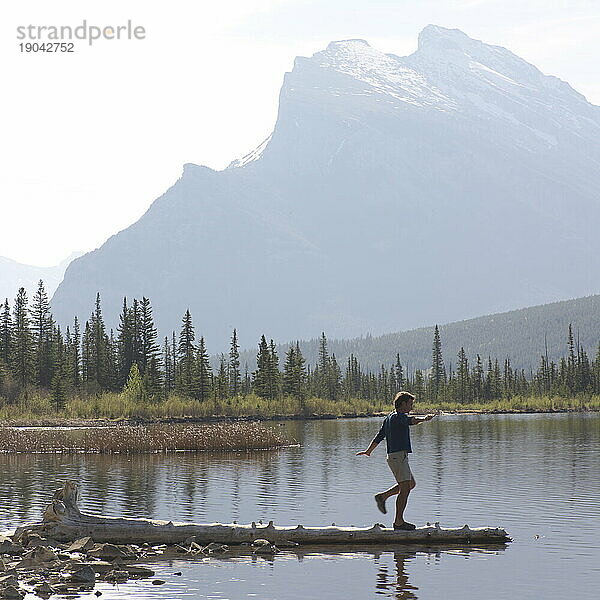 Mann balanciert entlang eines Baumstamms in einen Alpensee  dahinter Mount Rundle