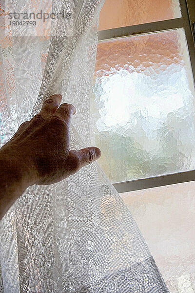 Eine Hand  die Spitze am offenen Fenster hält.