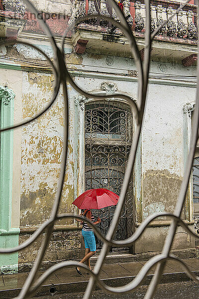 Eine junge kubanische Frau geht mit einem roten Regenschirm durch den Regen. Santa Clara  Kuba