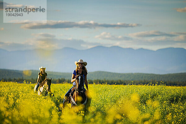 Zwei Cowgirls reiten durch ein Rapsfeld in Montana