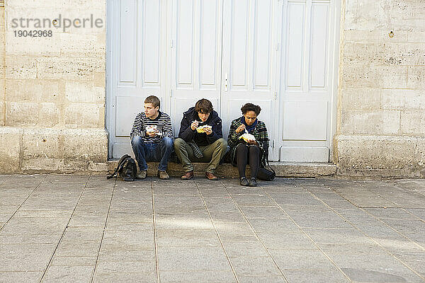 Drei junge Leute essen  während sie auf einer Stufe sitzen.