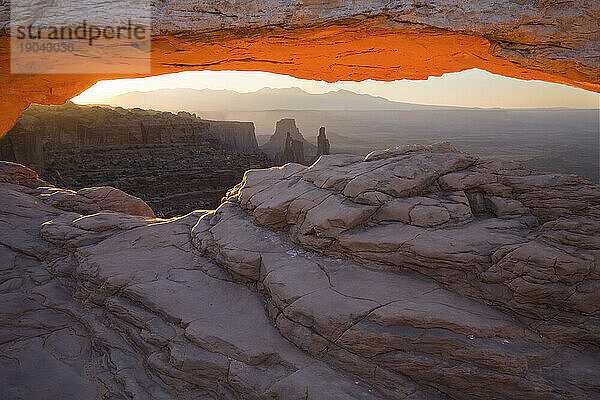 Der Mesa Arch im Canyonlands-Nationalpark in Utah leuchtet orange  während die Morgensonne durch diese beliebte Felsformation bricht