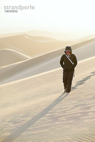Einsame Frau in schwarzer Puffjacke geht allein in der Wüste spazieren