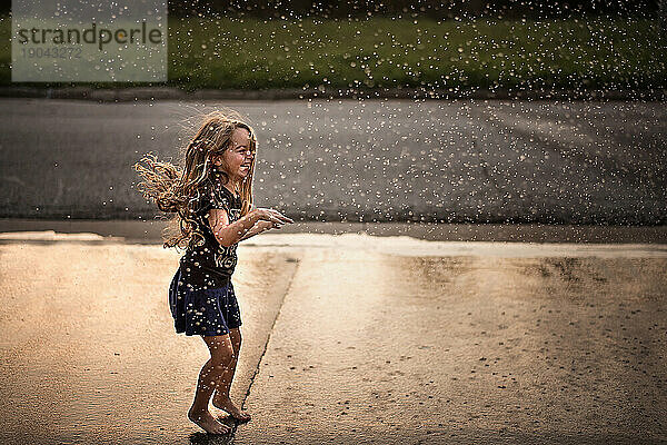Kleines Mädchen springt und lacht im Regen