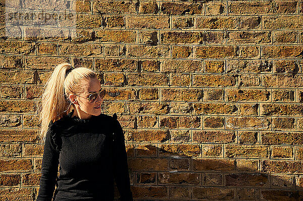 Attraktive junge Blondine steht neben einer Mauer