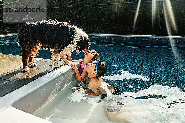 Junge und Mädchen küssen ihren Hund an einem heißen Sommertag am Pool