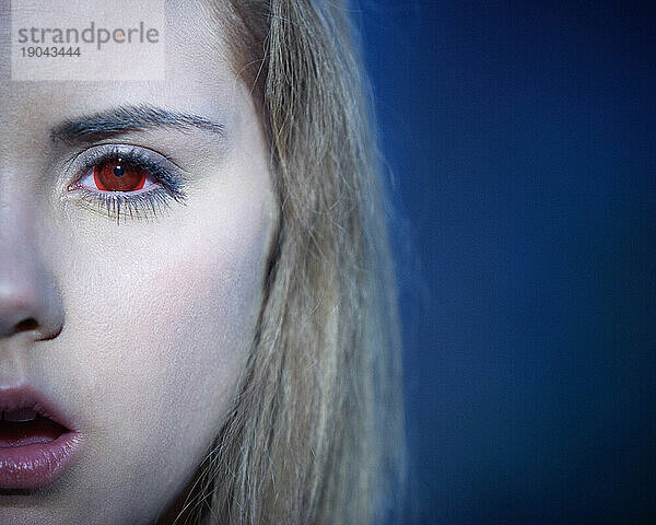 Ausgeschnittene Vorderansicht einer Frau mit roten Kontaktlinsen  die in die Kamera starrt.