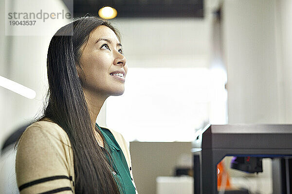 Seitenansicht einer lächelnden  nachdenklichen Geschäftsfrau  die wegschaut  während sie im Büro steht