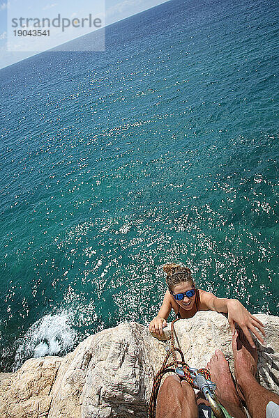 POV mit einer jungen Frau  die einen senkrechten Felsen über dem Meer erklimmt