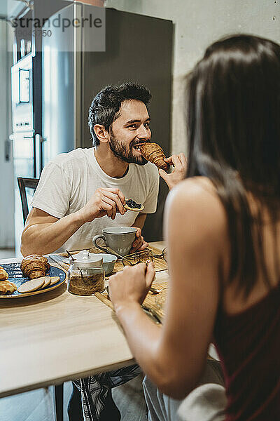 Junges glückliches verliebtes Paar beim Frühstück am Küchentisch