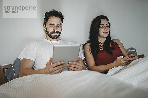 Junges Paar im Bett mit Smartphone und Tablet