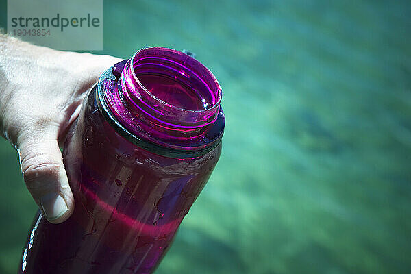 Eine Hand hält eine farbige Wasserflasche.