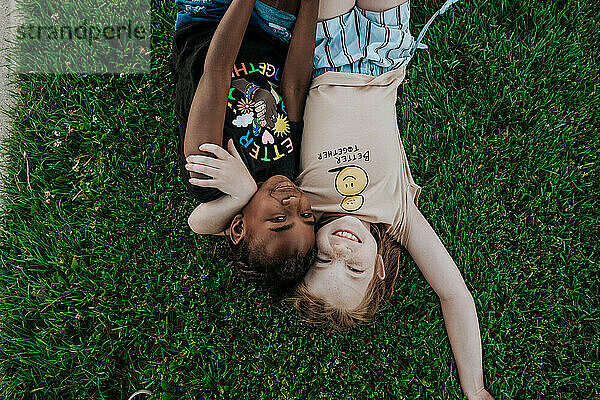 Zwei Mädchen liegen im Gras und umarmen sich und lächeln