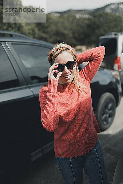 Rothaarige Frau passt schwarze Sonnenbrille in rotem Pullover und Jeans an