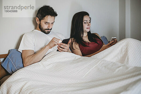 Junges Paar im Bett und schaut auf sein Smartphone