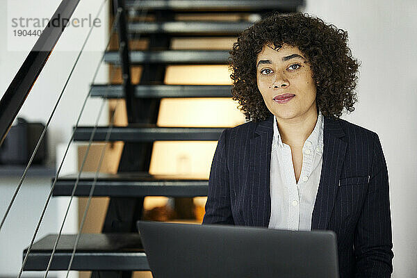 Portrait of confident businesswoman with laptop computer sitting on steps in office