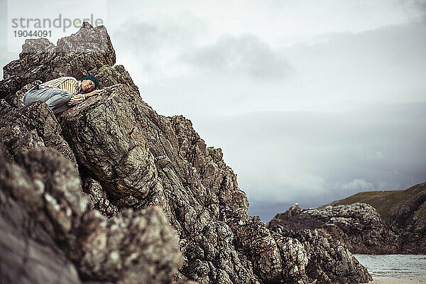 Person liegt auf Felsen an einem abgelegenen Strand in Schottland