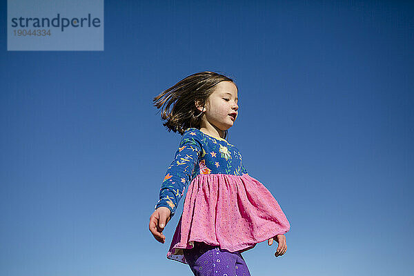 Obere Hälfte eines kleinen Kindes in leuchtenden Farben  das in einen blauen Himmel springt