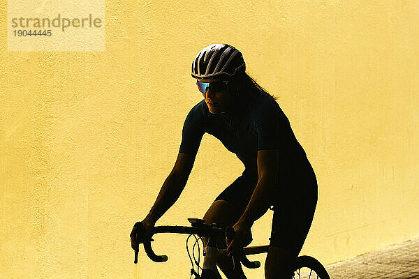 Minimalistische Silhouette einer Radfahrerin vor einer schlichten gelben Wand