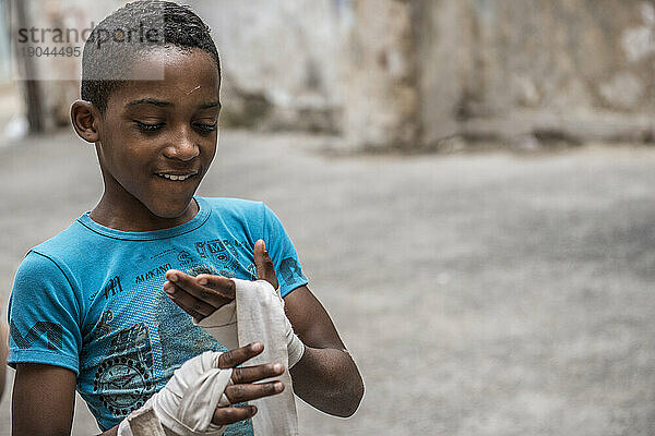 Ein junger kubanischer Junge sieht glücklich mit seinen Boxbandagen aus  als er sich auf das Sparring beim Project Cuba Boxeo  Alt-Havanna  La Havanna  Kuba  vorbereitet